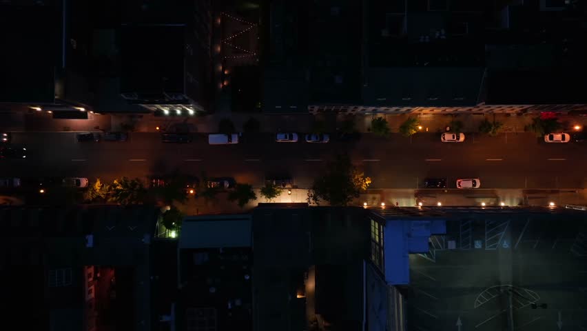 Driving cars on main street of small town at night. American housing area with warm lighting streetlights. Aerial top down tracking shot.