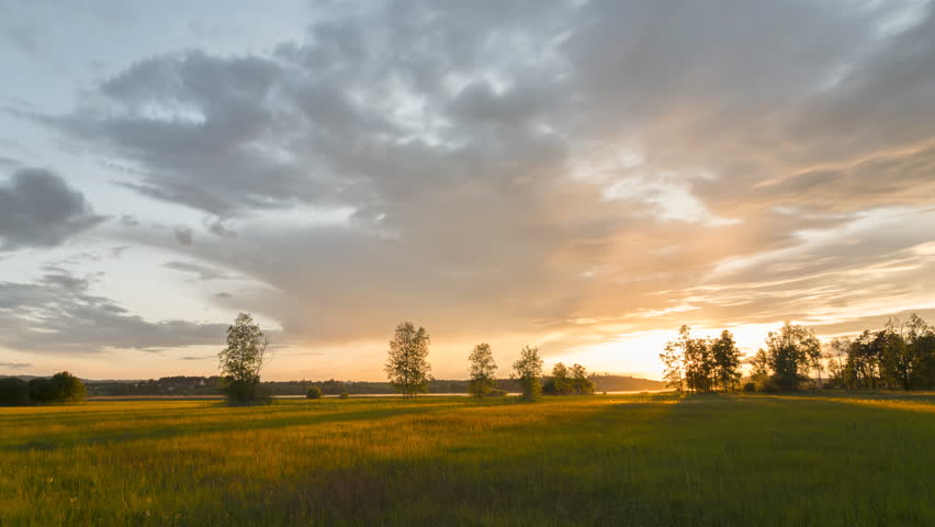 Sunset light recedes across grassy field as clouds race across soft smooth sky