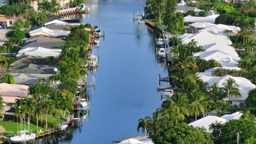 Aerial wide shot of luxury villas in Boca Raton City during sunny day in Florida. Real estate neighborhood with private river. Downtown skyscraper in background.