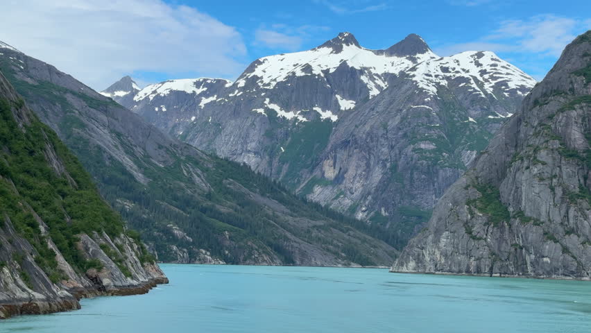 Passing view (from a cruise ship) of mountain peaks with snow and ice beyond a bend in Tracy Arm fjord in southeastern Alaska, for motifs of wilderness, extreme terrain, summer travel
