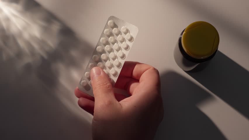 Hand Holding Blister Pack of Pills with Medicine Bottle. Close-up, shallow dof.