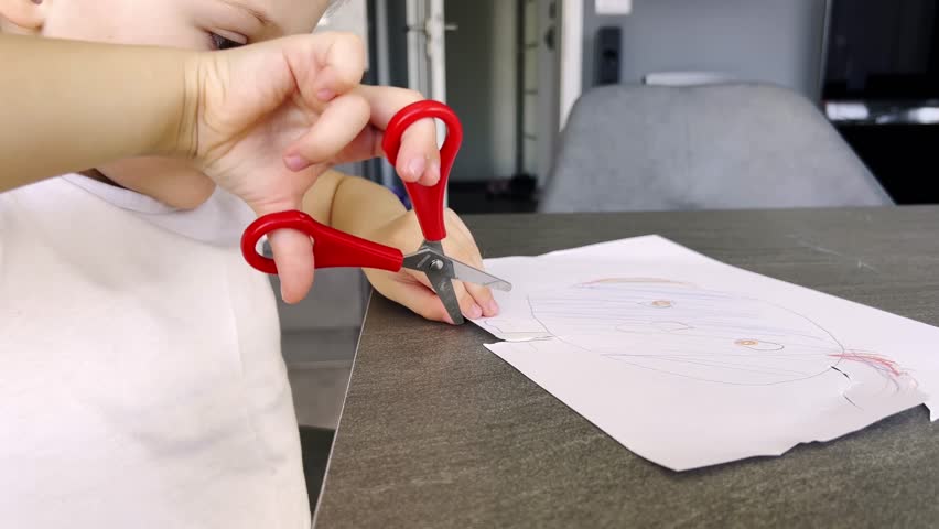 Little girl cuts out a shape from paper with scissors. Activities with children at home. High quality 4k footage