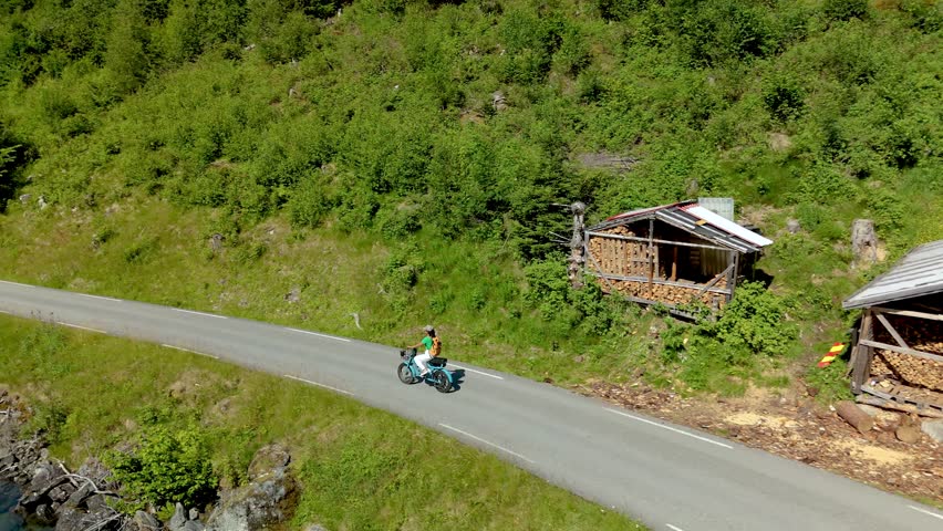 A peaceful women on a ebike ride on a coastal road surrounded by lush forests and clear blue waters on a sunny day. Lovatnet, Norway