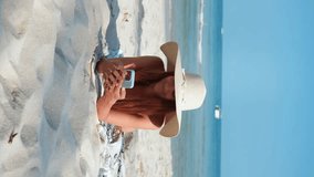 Vertical video woman sunbathes on beach tropics and chats using mobile phone. Millennial enjoy beauty of sea and beach while correspond using chat app. Using smartphone to communicate during holidays. - Powered by Shutterstock - Get 15% off with code: PIKWIZARD15