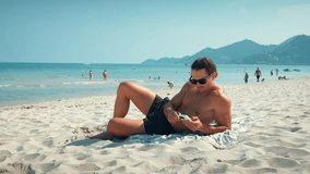 Man sunbathes on beach, reading messages on mobile phone. Millennial responds to messages without forgetting to enjoy beauty of ocean. Messages allow to stay in touch even while in piece of paradise. - Powered by Shutterstock - Get 15% off with code: PIKWIZARD15