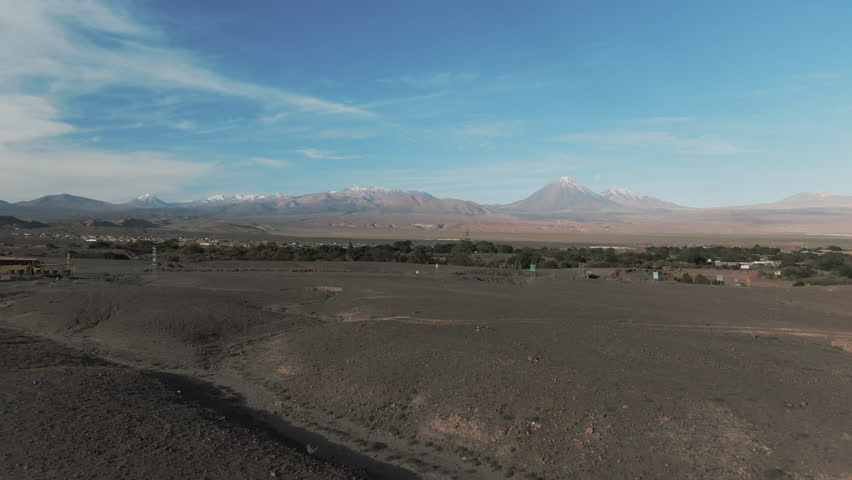 Aerial: Drone Panning Shot Of Vehicles Moving By Snowcapped Mountains, Drone Flying Over Semi Arid Desert Landscape On Sunny Day - Atacama Desert, Chile