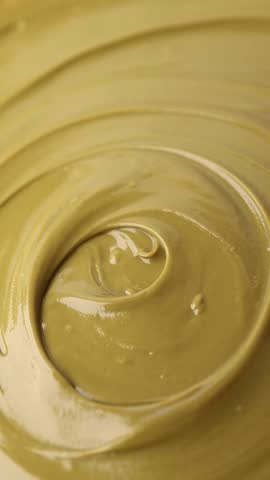 pistachio paste, rotation in circle. Pistachio cream, Turning. selective focus. green background. Vertical video