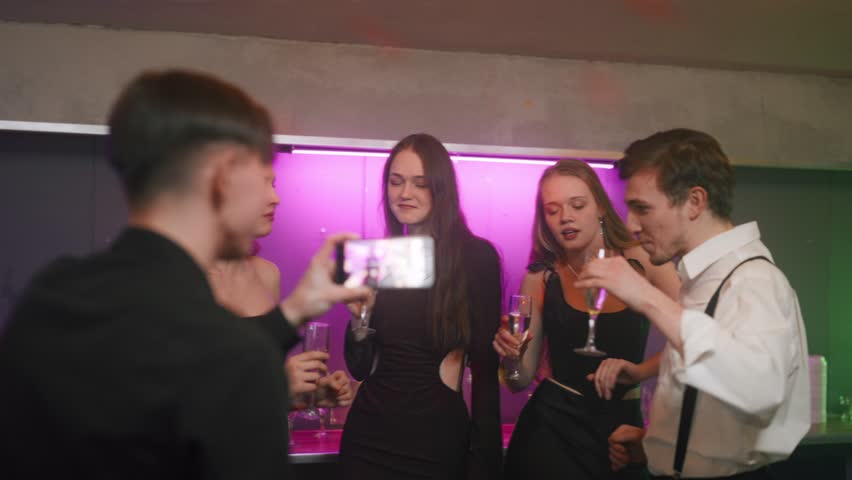 Joyful friends taking selfie by smartphone in merry party in Christmas night. Happy beautiful women and handsome men smiling to frontal camera of mobile phone, people have fun in classmates meeting