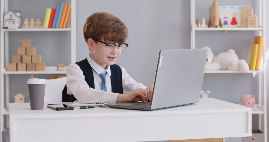 Funny happy smiling preschool child boy businessman wearing suit and glasses working on laptop sitting at the desk in office. Little cute boss entrepreneur working on workplace. 4k video.