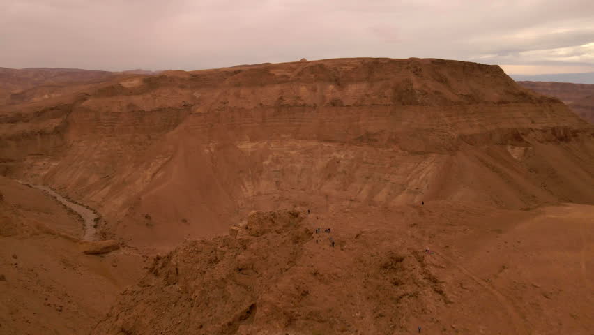 Aerial Forward Shot Of Steep Rock Formations Surrounding Wadi Under Cloudy Sky - Mitzpe Ramon, Israel