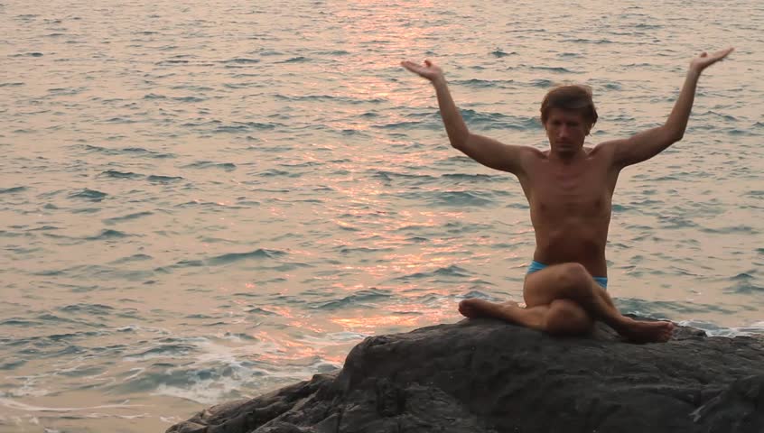 Young man doing yoga exercise on the deserted wild stone sea beach (HD)