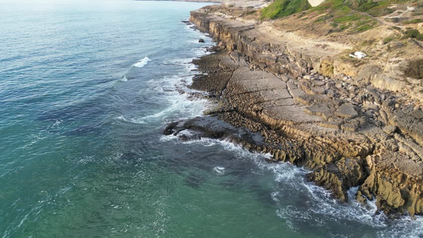 high-definition video captures a static drone shot from a top-down perspective of waves crashing onto rugged rocks along the shoreline