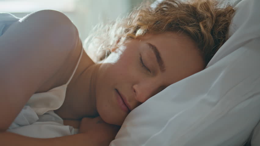 Portrait beautiful girl waking up in morning. Sleepy woman opening eyes looking camera in bedroom. Smiling curly model sleeping on cozy pillow dreaming on peaceful weekend. Lifestyle beauty concept