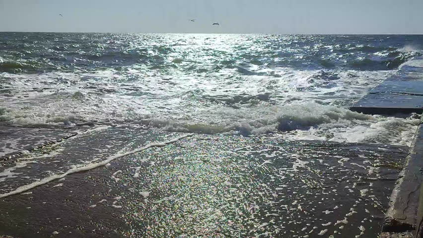 Storm. Storm at sea. Large high sea waves with white foam hitting concrete pier wall and splashing on hot sunny summer day. Stormy sea weather. Rough sea. Shore and waves. Nature. Natural background