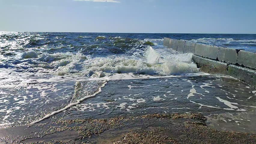 Storm. Storm at sea. Large high sea waves with white foam hitting concrete pier wall and splashing on hot sunny summer day. Stormy sea weather. Rough sea. Shore and waves. Nature. Natural background