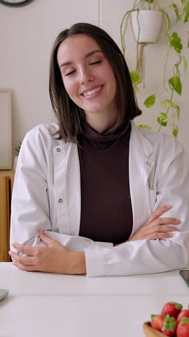 Vertical HD video. Portrait of young beautiful nutritionist woman smiling at camera at medical consultation. Professional healthcare worker concept