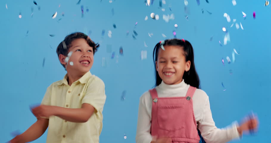 Fun, friends and children in studio with confetti for kids party, happy winning or prize giveaway. Congratulations, excited boy and girl dancing in celebration with glitter, smile and blue background