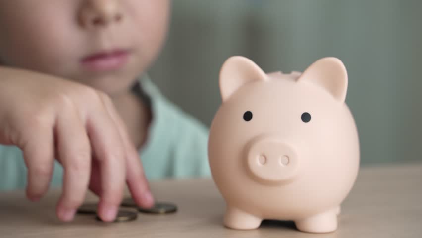A young child is learning about financial literacy by dropping coins into a piggy bank. Concept of financial literacy from an early age
