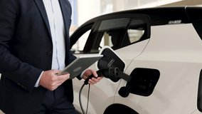 Business professional displaying electric car at vehicle dealership. Hand connecting charging cable to electric vehicle highlighting eco-friendly transportation options. - Powered by Shutterstock - Get 15% off with code: PIKWIZARD15