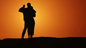 A couple is standing on a hillside, silhouetted against a beautiful sunset - Powered by Shutterstock - Get 15% off with code: PIKWIZARD15