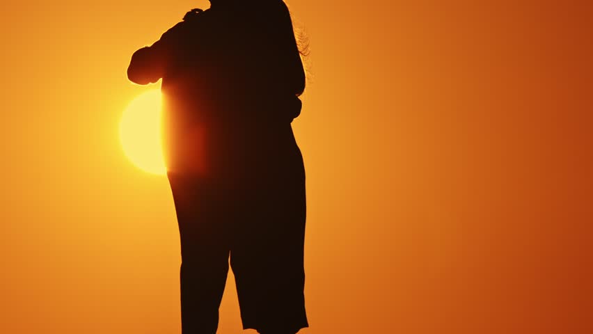 A couple is dancing silhouetted against a sunset