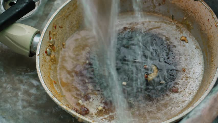 Young woman washes a pan in the kitchen after finishing cooking.