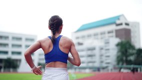 A woman runs on a track with a blue tank top on. The sky is cloudy and the buildings in the background are white - Powered by Shutterstock - Get 15% off with code: PIKWIZARD15