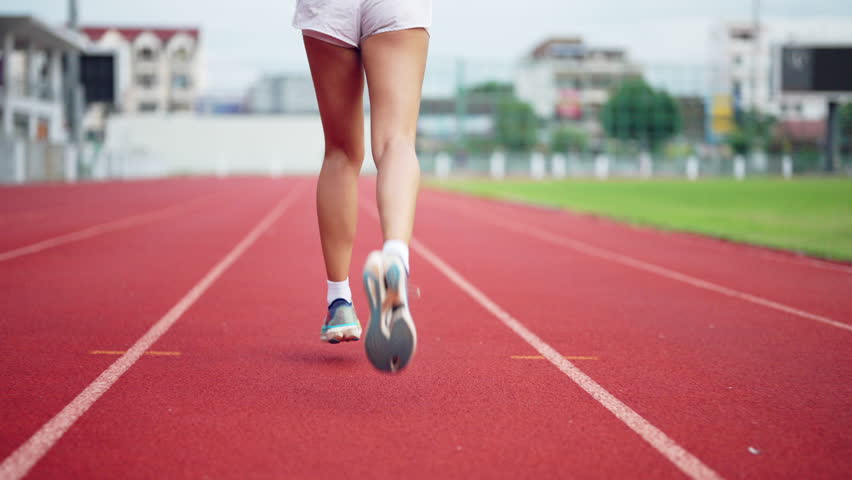 A woman runs on a track with her legs apart. She is wearing white shorts and a white shirt