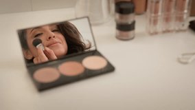 Smiling happy Caucasian woman looking reflection mirror blush palette table female girl model artist putting cosmetics makeup brush apply powder shadows visage product on face blog beauty home studio - Powered by Shutterstock - Get 15% off with code: PIKWIZARD15
