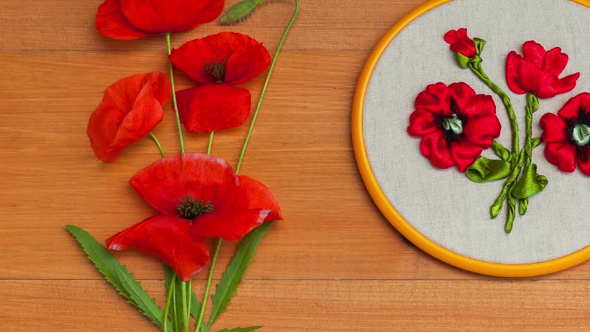 Video of floral hand embroidery with satin ribbons of red poppy flowers in hoops on wooden background. Crafts and embroidery as hobby and leisure. Top view, close-up, flat lay, mock up