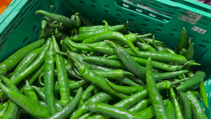 Fresh green chili peppers in a green plastic basket at a local market. High quality 4k video.