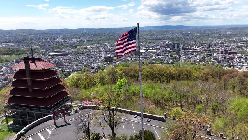 American flag waving on top of hill near Pagoda Building in Reading City. Small american town in the valley. Aerial passing by top down.