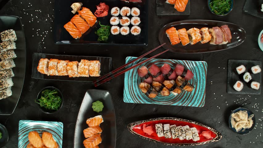 Top view of traditional japanese cuisine . Sushi rolls set with salmon , tuna fish and vegetable served on black stone table . Asian food on black stone slate with chopsticks . Camera movement .