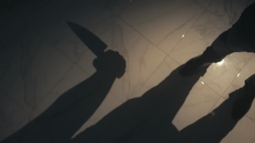 The shadow of a person holding a knife is cast on the floor, creating a suspenseful and ominous atmosphere. The image evokes themes of danger, mystery, and tension.