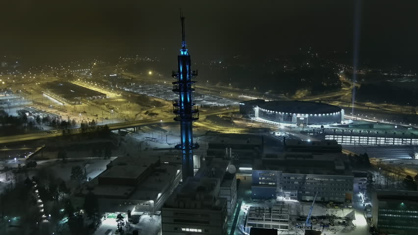 Helsinki.Finland-December 31.2021: High angle view showing Pasila Helsinki and the tv tower during nighttime. Lights. Snowfall. Wintertime. Beautiful cityscape. Drone slowly moving backwards.