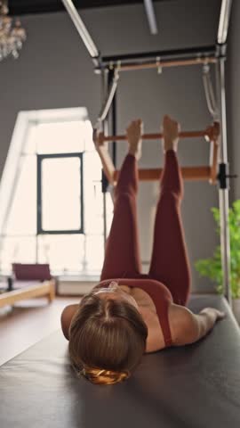 Woman doing pilates exercises on Balanced Body Cadillac machine at studio, focusing on strength and flexibility