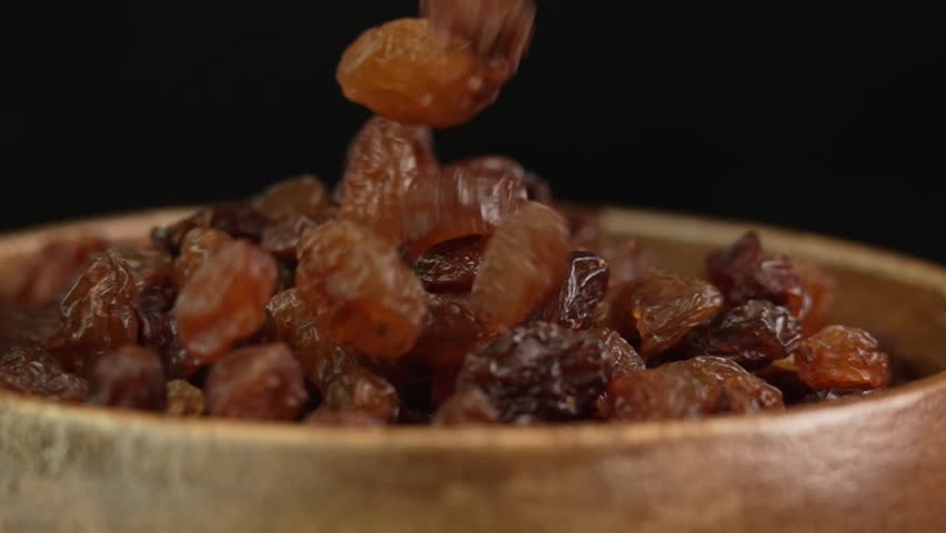 Black raisins slowly fall into a wooden bowl in slow motion. Dried grapes close-up. Dried fruits and dry berries