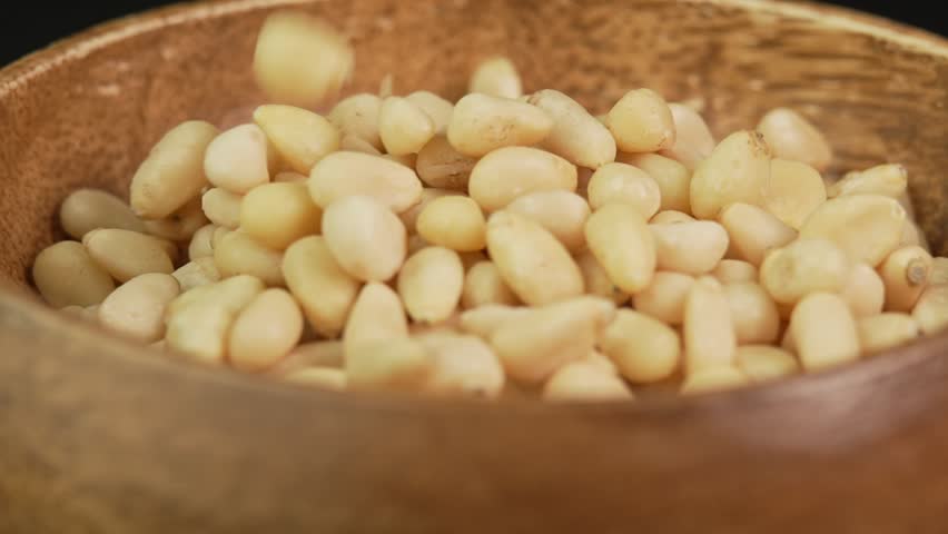 Peeled pine nuts are poured into a wooden bowl in slow motion. Pine nut kernels close up. Healthy nut