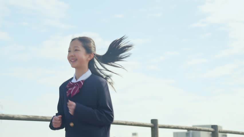 A girl in a school uniform running under the blue sky.