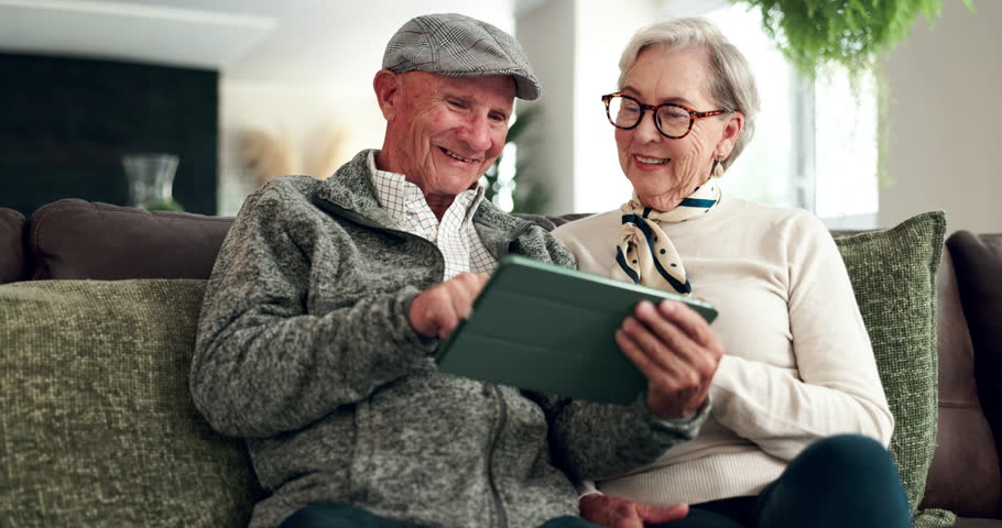 Senior, couple and laughing with tablet in home, happy and social media in retirement or people together on sofa. Relax, bonding and streaming funny videos online, living room and connection in house