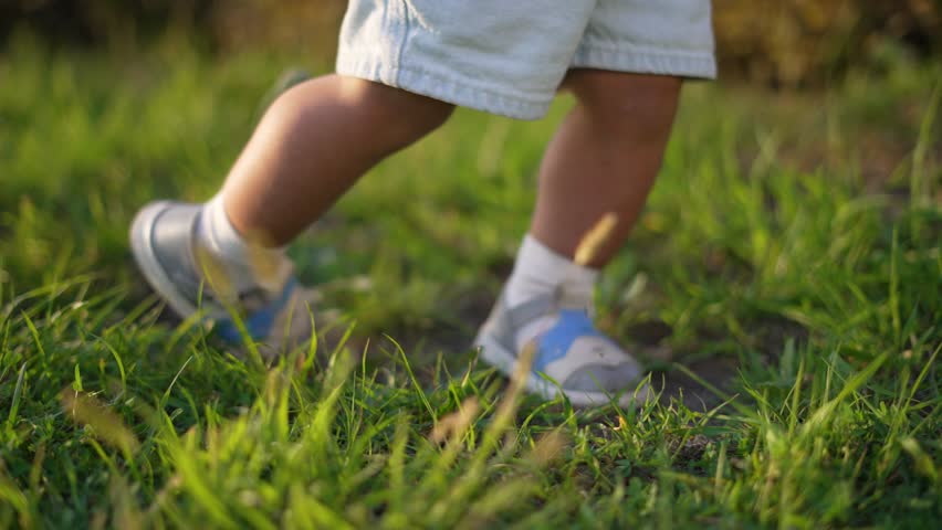 Mother helps baby take steps on grass. Baby learning to walk outdoors. Happy bonding time with mother. Baby's first steps in nature. Baby, step, grass, mother moment. Happy family in the park