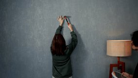 Confident brunette girl hammers a nail into the wall and hangs a clock on it with the support of her boyfriend in a modern apartment - Powered by Shutterstock - Get 15% off with code: PIKWIZARD15