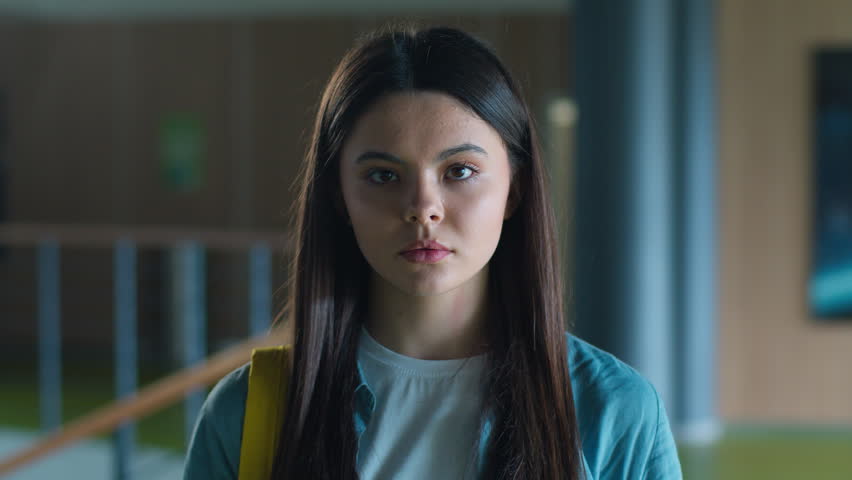 Portrait serious calm sad upset Caucasian student girl female schoolgirl woman pupil teenager teen teenage generation in school corridor in university college hall education study looking at camera