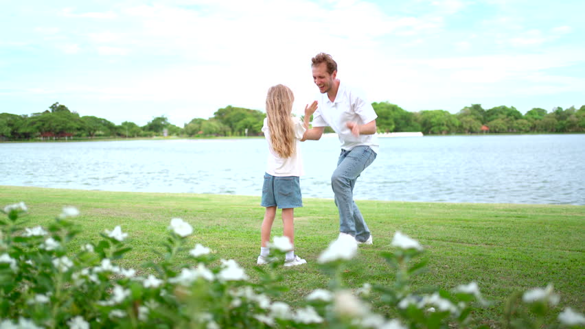 In a sunlit morning, Caucasian White Western father and his daughter are joyfully running and playing together in a field. Their laughter fills the air as they bask in the warmth of the early sun.