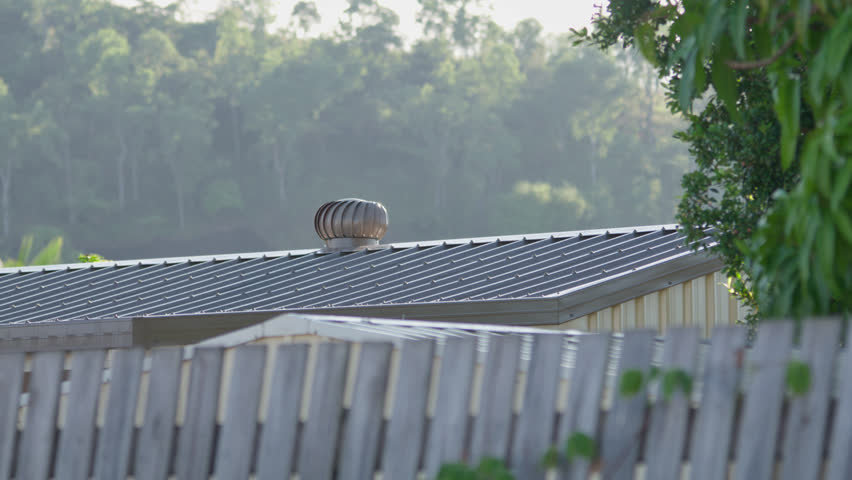 Pan Left, A metal shed with a whirlybird on its roof in the early morning sunlight with mountain terrain in background, Townsville, Queensland, Australia.
