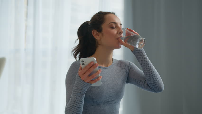 Caucasian slim fit woman female sportswoman smiling sport girl influencer using mobile phone app check result training workout at home drinking water healthy habit health care drink refreshing relax
