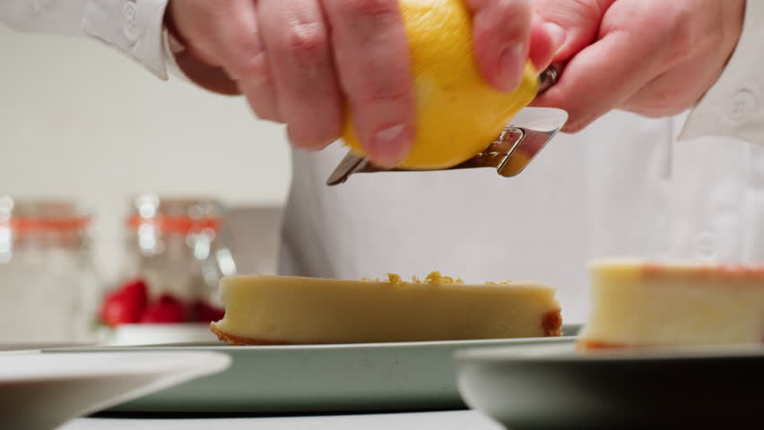 Pastry chef adding a lemon zest on classic dessert cheesecake close-up. Cheesecake is a dessert made with a soft fresh cheese , typically cottage cheese, cream cheese, quark or ricotta, eggs, and
