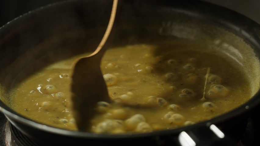Green boiling sauce texture close-up macro. Cooking green curry with wooden spoon at home.