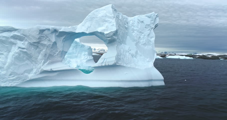 Polar climate change melting icebergs in Antarctica. Huge hole cave arch window melted ice wall drifting Antarctic ocean close up. Arctic winter landscape, global warming problem. Drone shot zoom in