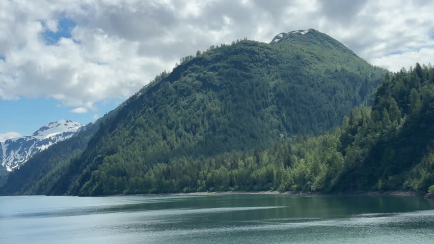 Panning view of scenic wilderness, with surrounding mountains, in Glacier Bay National Park and Preserve in southeastern Alaska on a partly cloudy afternoon early in summer